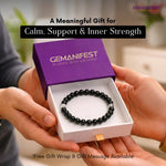 Black beaded bracelet in a 'GEMANIFEST' box held by hands with blurred background