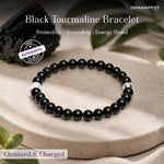 Black tourmaline bracelet on a stone surface with GEMANIFEST branding.