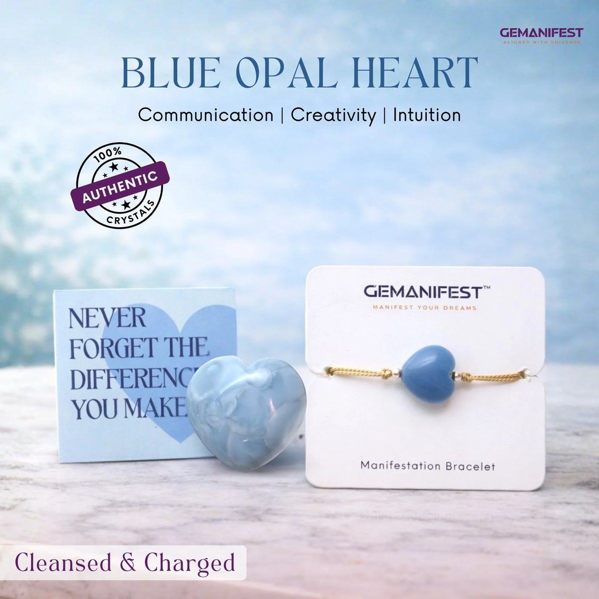 Blue opal heart crystal on a card with 'GEMANIFEST' branding against a blurred natural background.