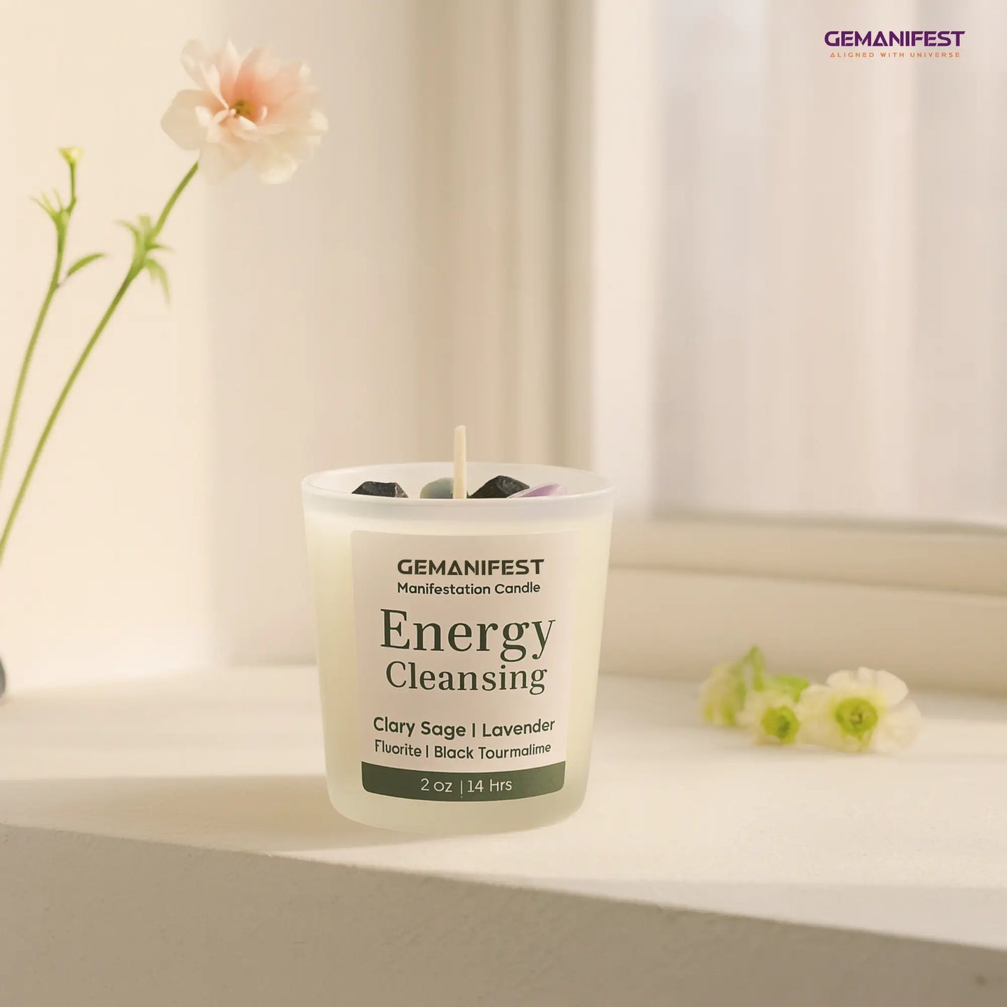 GEMANIFEST Energy Cleansing candle on a surface with flowers in the background