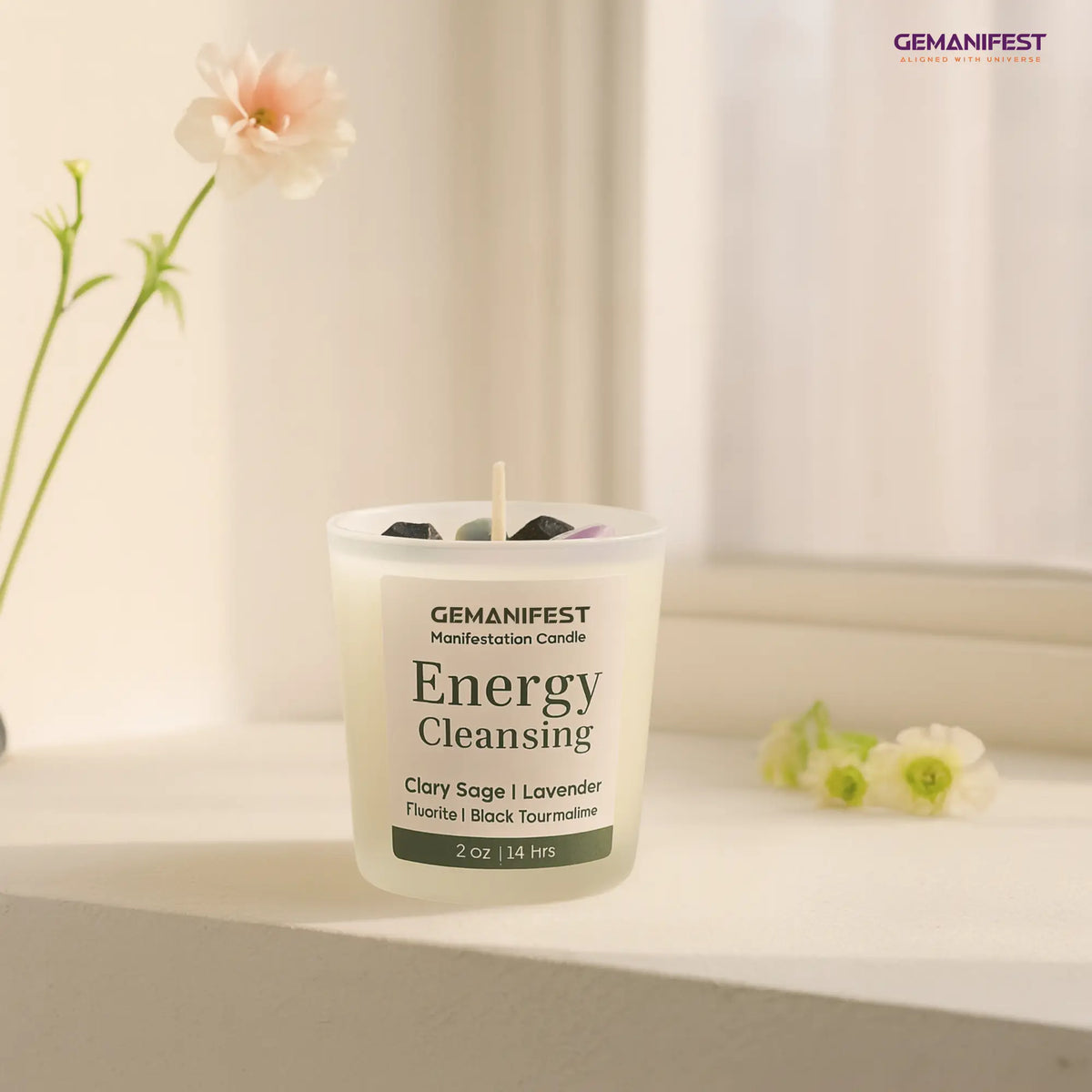 GEMANIFEST Energy Cleansing candle on a surface with flowers in the background