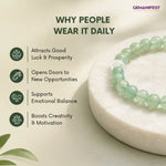 Green beaded bracelet on a white stone with GEMANIFEST branding and benefits listed.