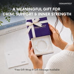 Person holding a GEMANIFEST-branded gift box with a bracelet, surrounded by books on a light surface.