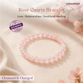 Rose Quartz bracelet on a soft fabric background with flowers, featuring GEMANIFEST branding.