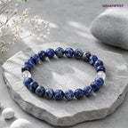 Blue beaded bracelet on a stone surface with 'GEMANIFEST' branding.
