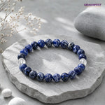 Blue beaded bracelet on a stone surface with 'GEMANIFEST' branding.