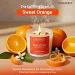 Gemanifest candle with sweet orange scent surrounded by oranges and leaves on a wooden surface.
